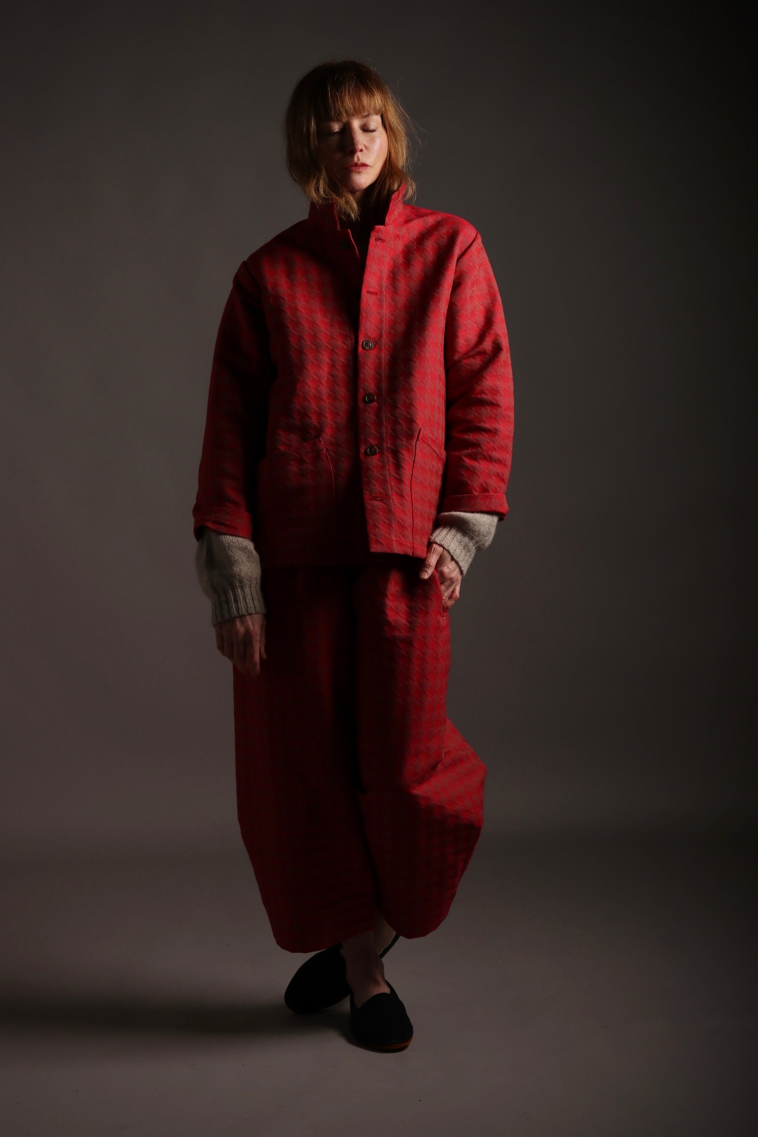 Sienna wears comfortable baggy trousers and simple five button jacket with patch pockets in red cotton with a houndstooth pattern.